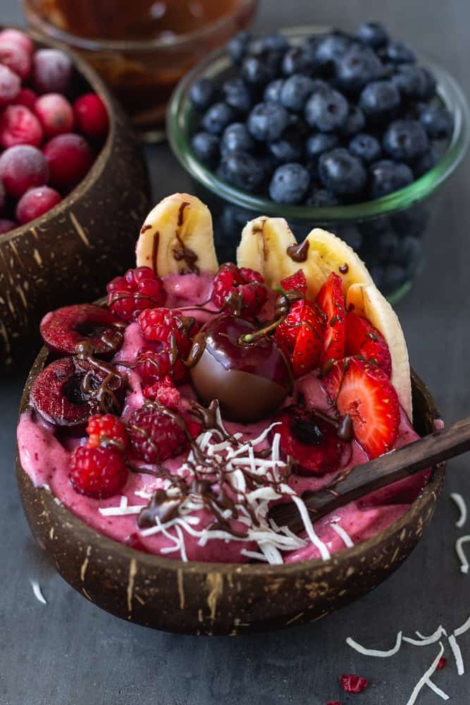 Vegan cherry ice cream topped with summer berries, bananas, and chocolate covered cherries in a coconut bowl.