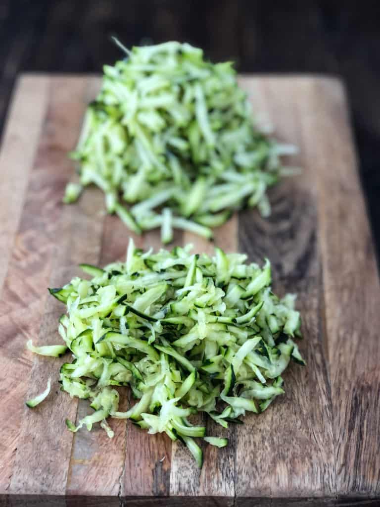 Piles of grated zucchini on a cutting board.