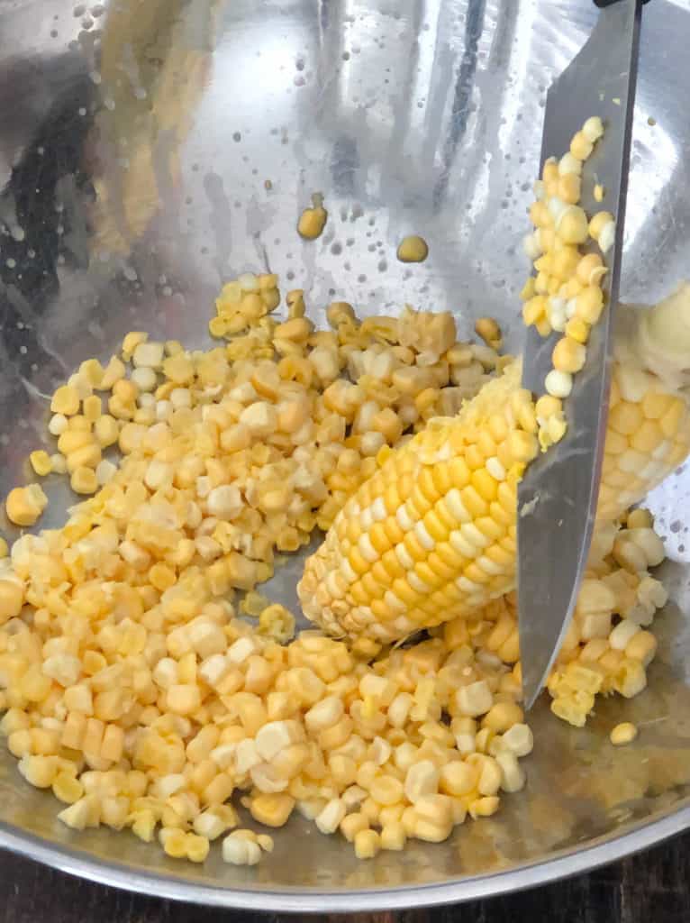 Corn being cut off the cob into a large mixing bowl.