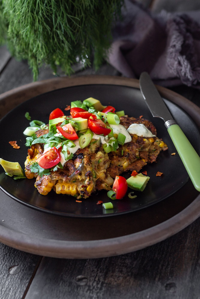 Plate of vegan corn fritters topped with tomato, avocado and green onions.