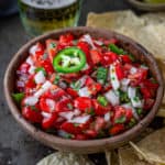 Bowlful of pico de gallo on a tray of taco chips and a glass of beer.