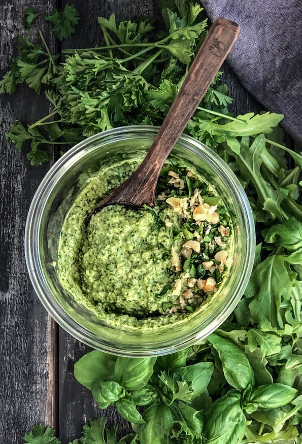Vegan basil pesto in a jar surrounded by basil and parsley.