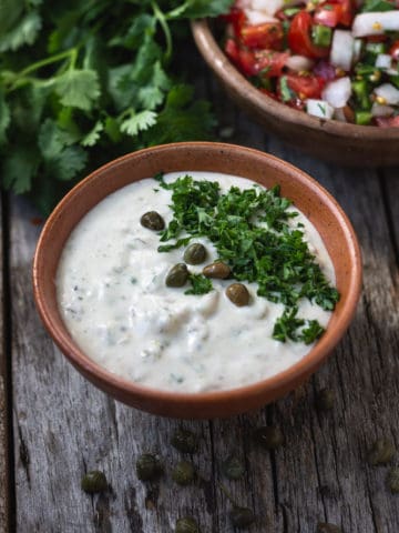 Vegan tartar sauce in bowl topped with capers and chopped parsley.