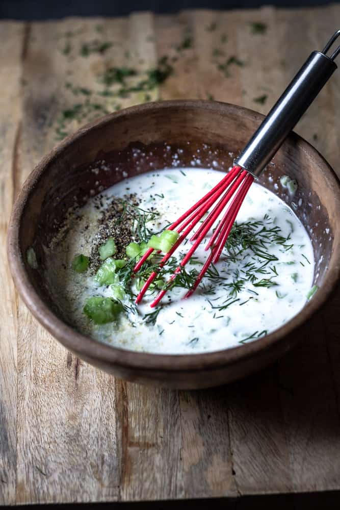 Bowl of creamy, dairy-free tzatziki sauce being whisked with lemon juice.