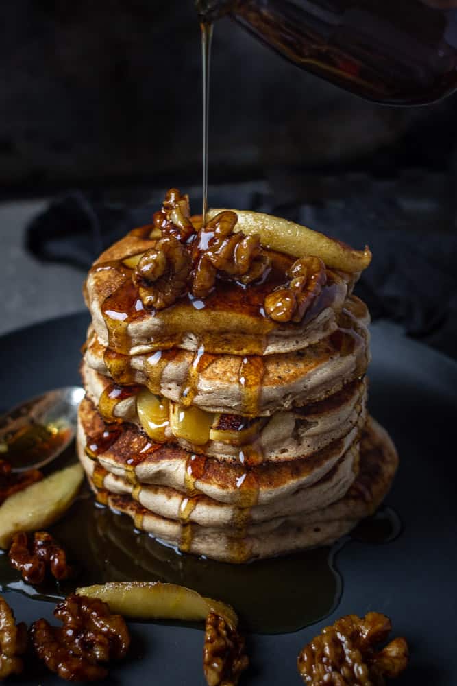 Stack of apple pancakes topped with walnuts and syrup drizzles.