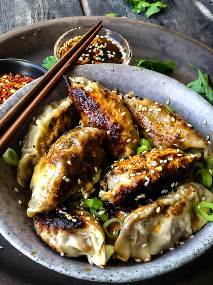 Bowlful of vegan potstickers/dumplings with spicy maple dipping sauce.