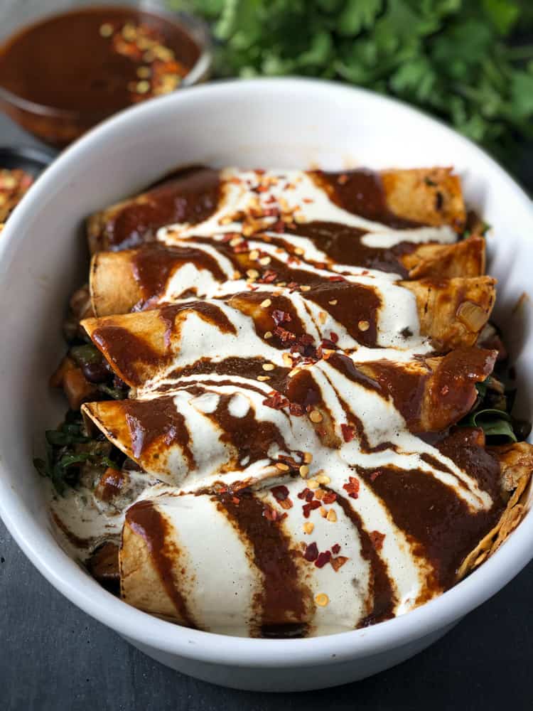 Baking dish filled with vegan enchiladas covered in white sauce and spicy enchilada sauce.