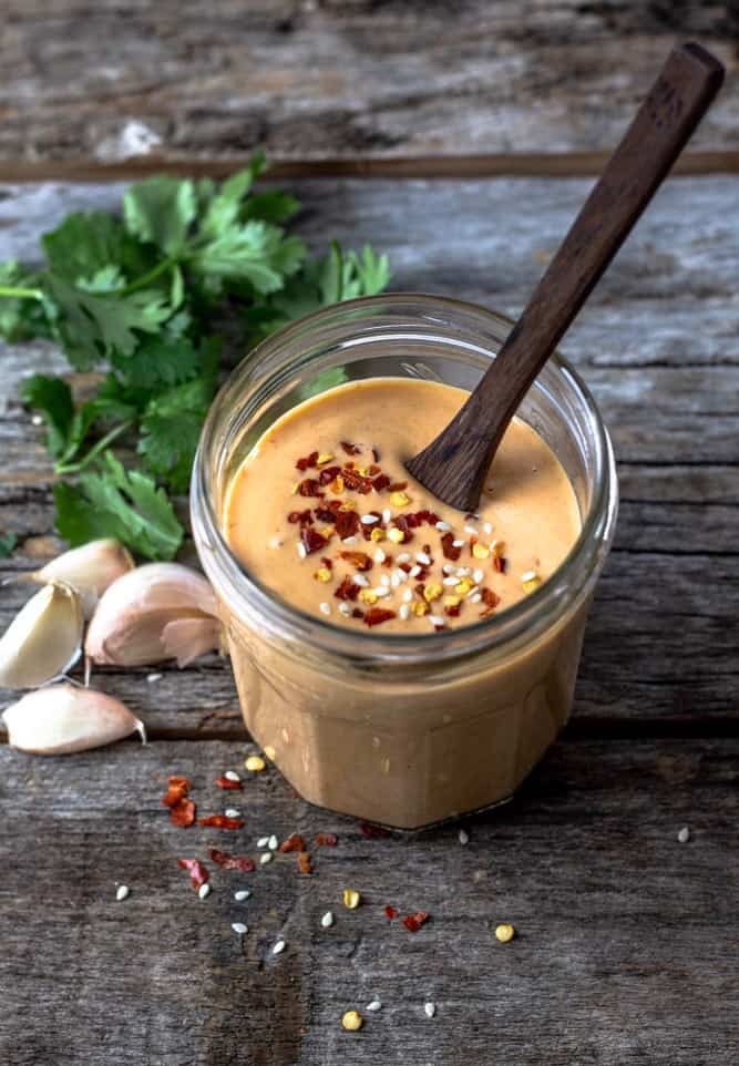 thick, orange, sweet and spicy tahini sauce on a serving board with garlic and greens