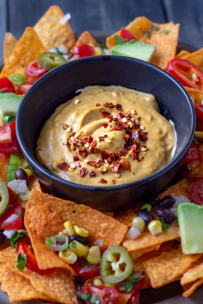 A bowlful of vegan queso cheese sauce on a tray surrounded by taco chips.