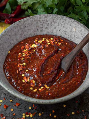 Bowlful of spicy red enchilada sauce with hot pepper flake garnish.