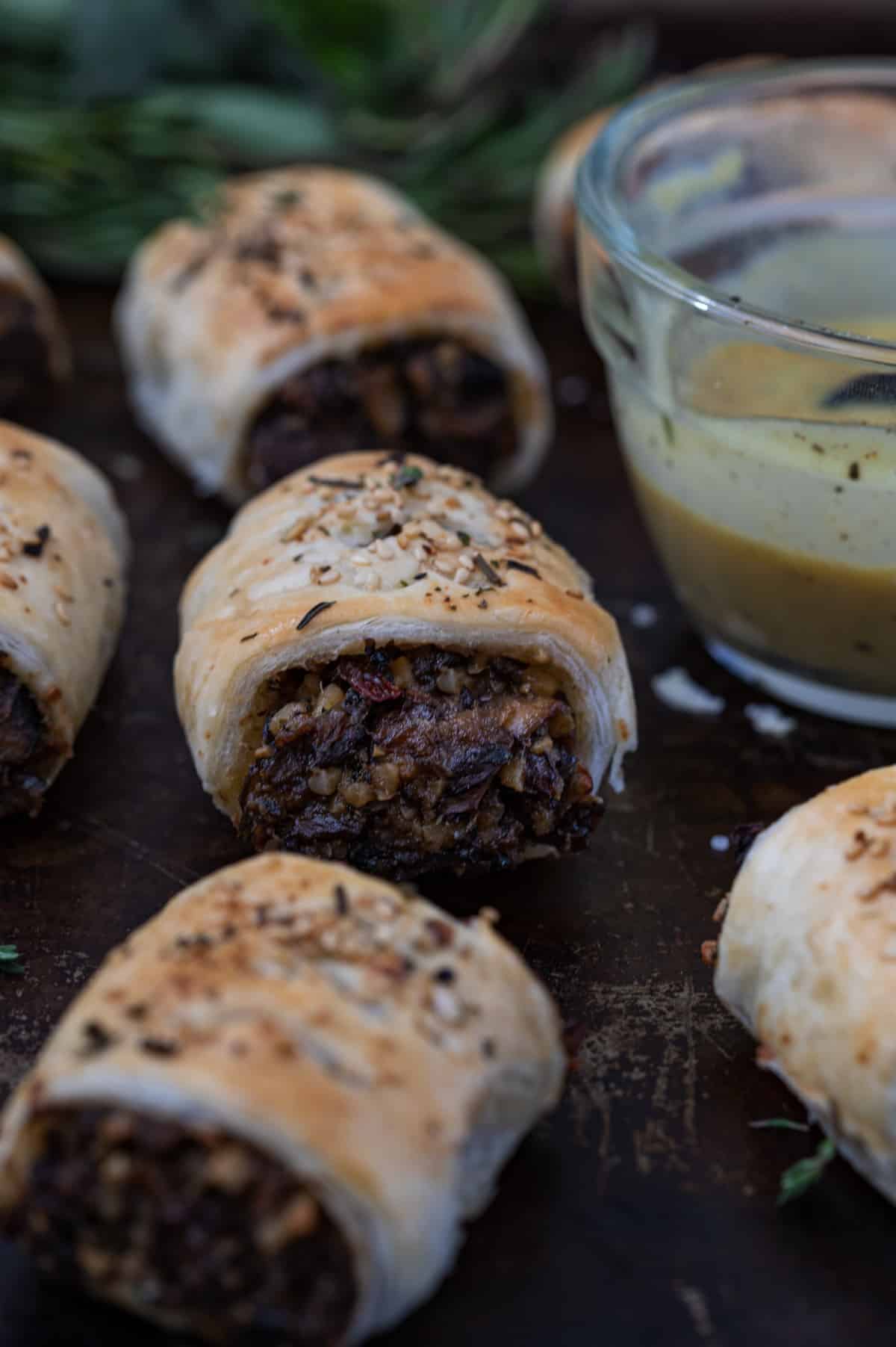 Flaky golden vegan sausage rolls on a baking sheet with sauce.