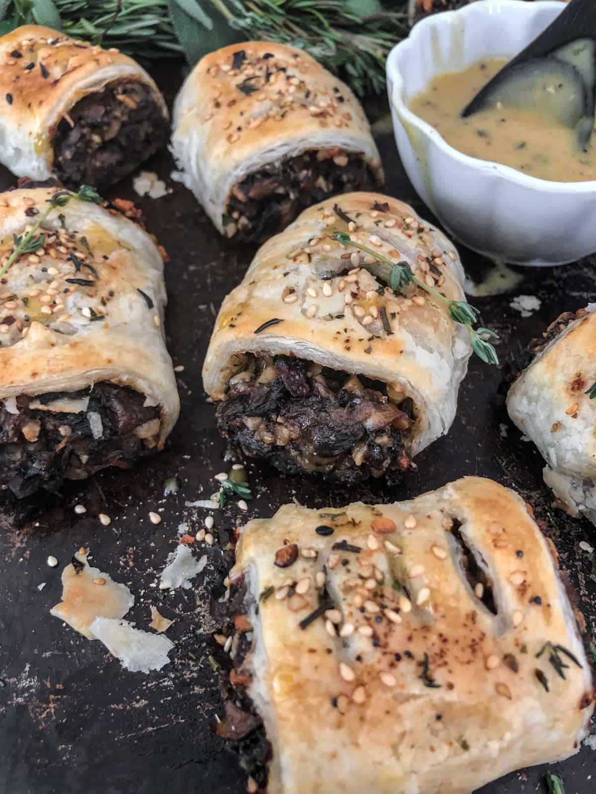 Flaky golden vegan sausage rolls on a baking sheet with sauce.