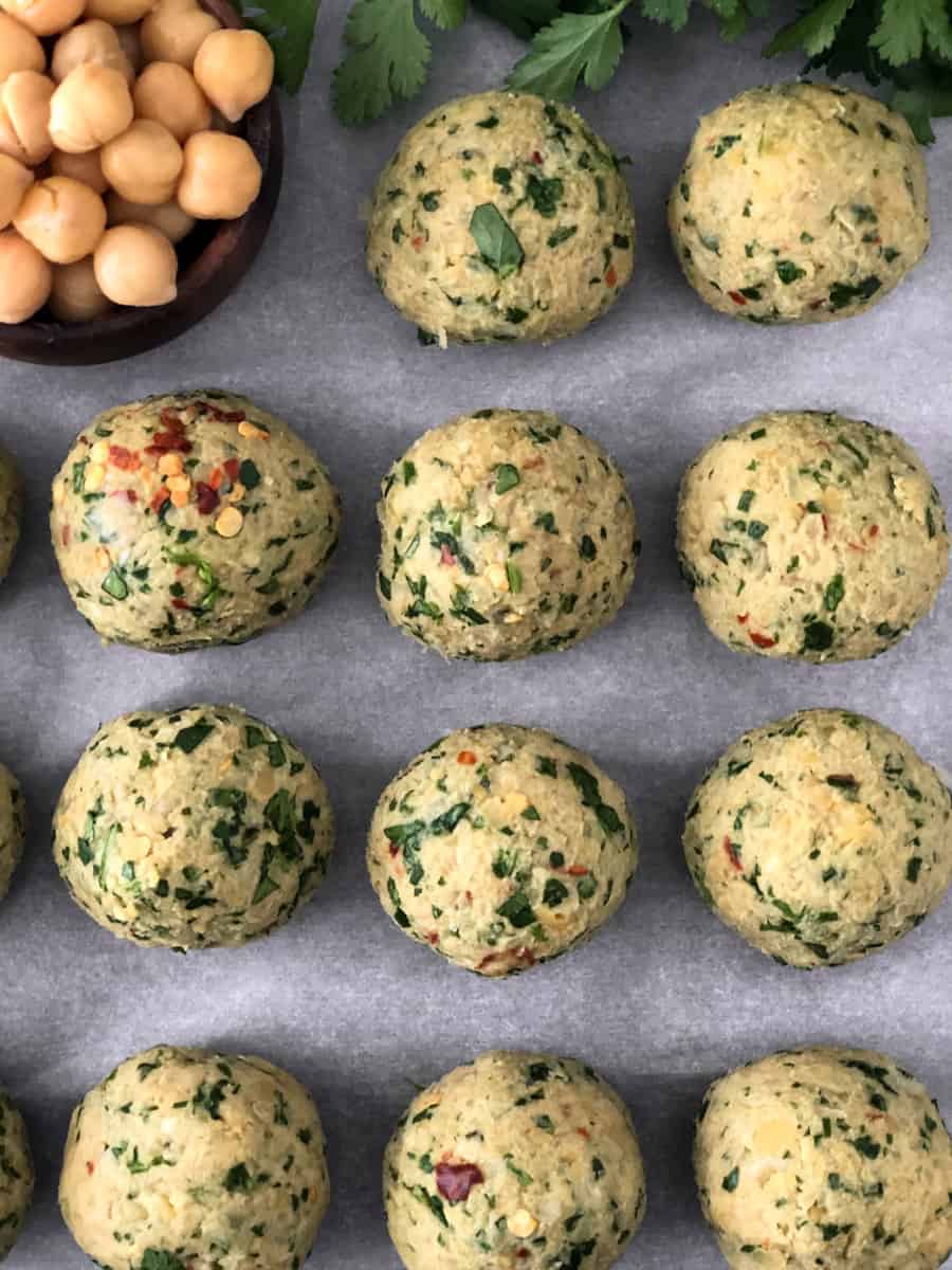 Falafel balls rolled on a baking sheet ready for the oven.