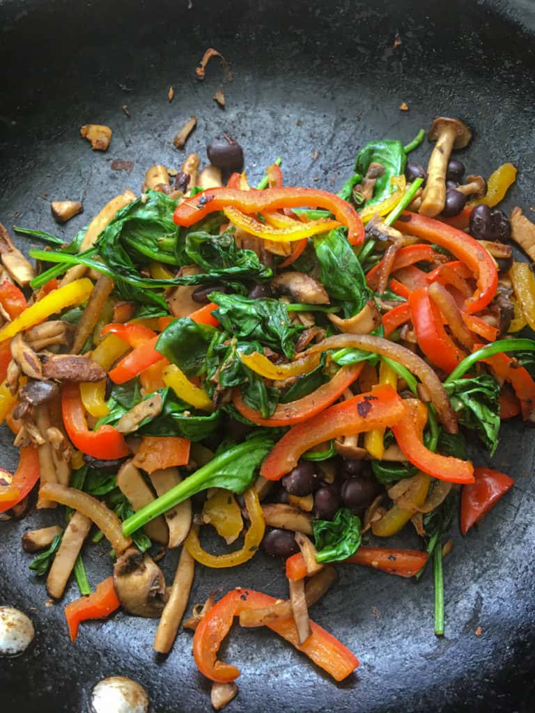 Peppers, spinach, mushrooms frying in a skillet.