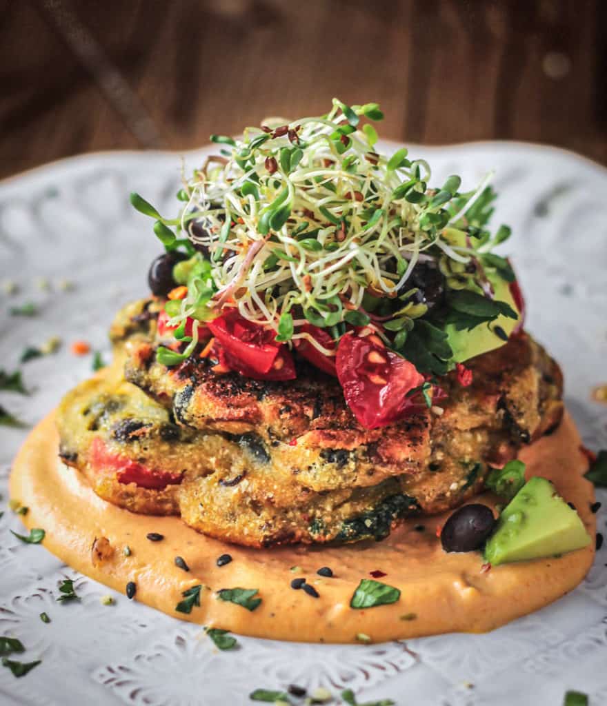 chickpea pancakes topped with avocado tomatoes and sprouts with spicy cashew drizzle