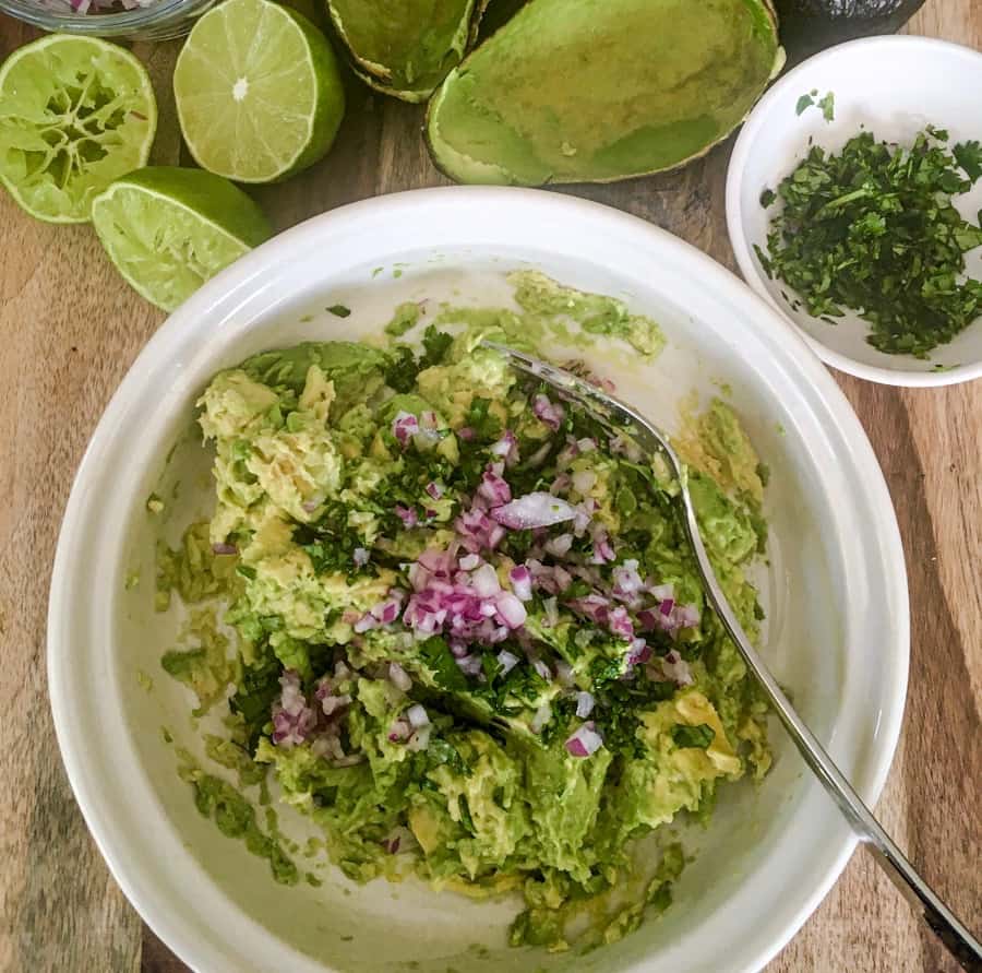 avocado guacamole in a bowl with limes and cilantro on a serving board