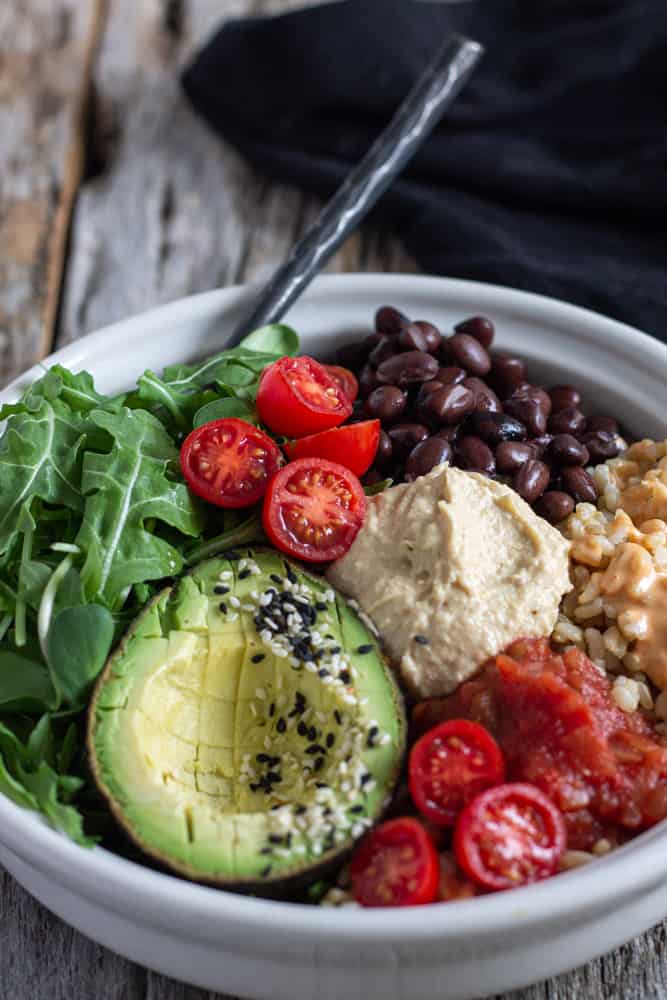 Tomato avocado bean and rice in a bowl with homemade hummus.