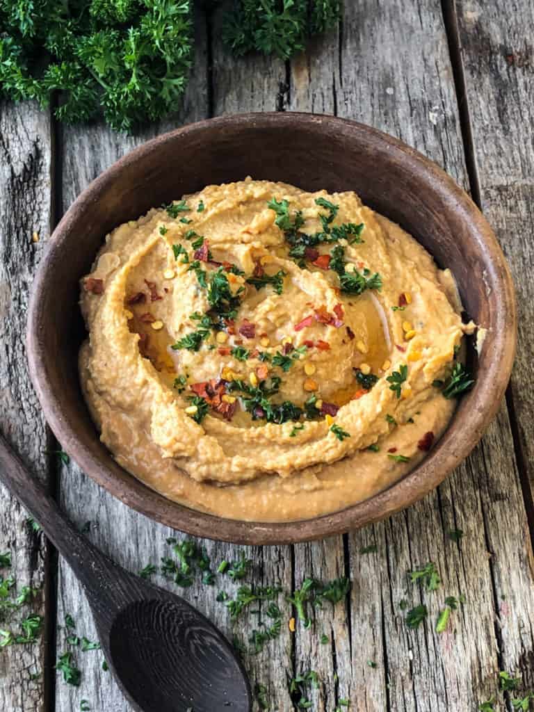 spicy hummus in a bowl with a sprinkle of parsley and hot pepper flakes