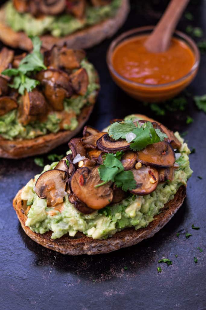 avocado toast with spicy mushrooms on top and extra spicy sauce on the side