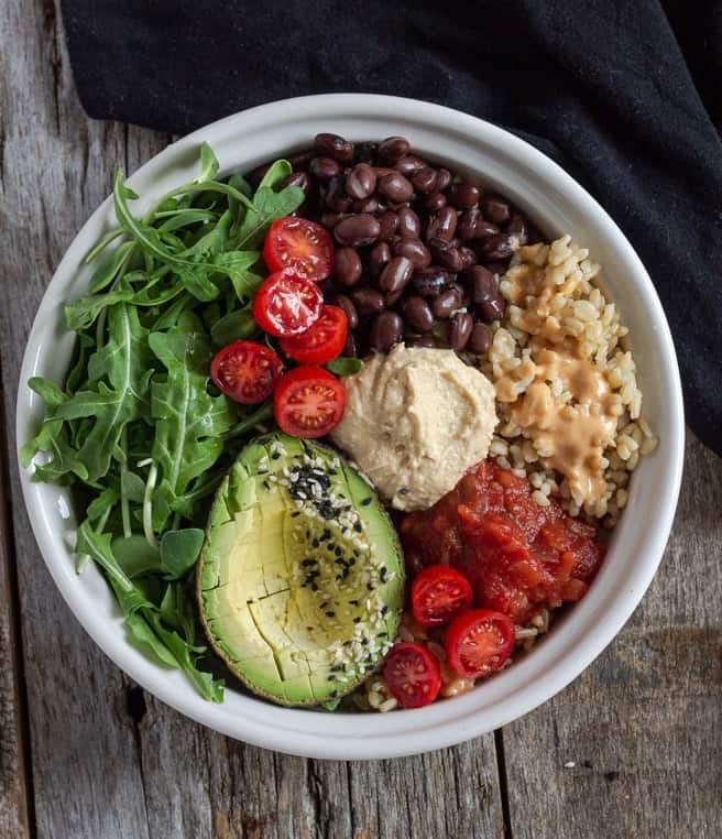 Spicy hummus in a buddha bowl with piles of rice, beans, greens, avocado and salsa.