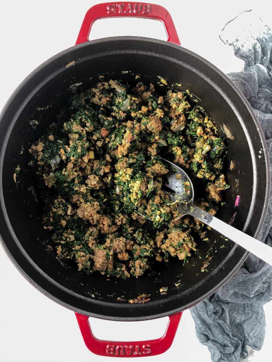 Meaty, spinach and onion mixture frying in a dutch oven. 