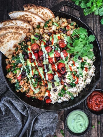 breakfast hash in a skillet with tomato and avocado and cashew drizzles