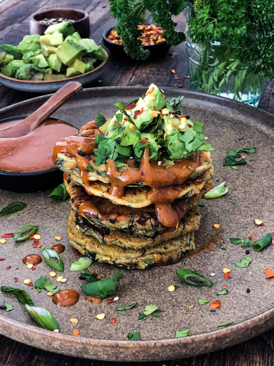Stack of green spinach pancakes on a plate with avocado and green onion topping.