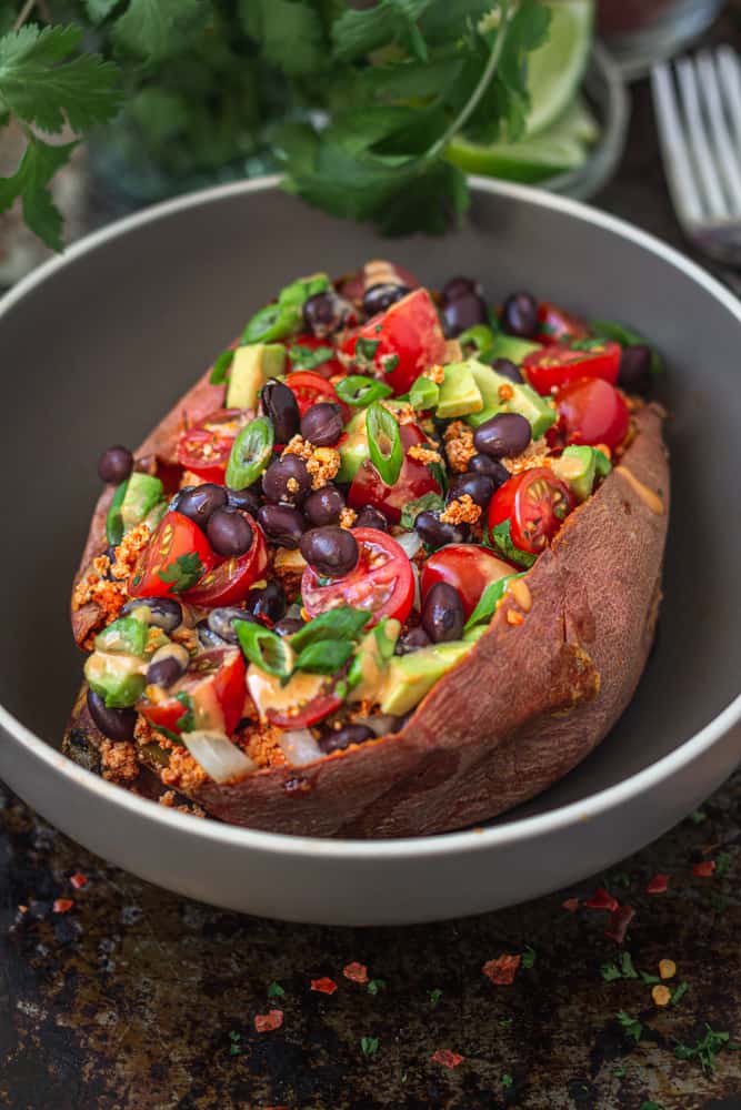 Taco flavoured tofu crumbles stuffed in a baked sweet potato with avocado, beans, and tomatoes, served in a bowl.