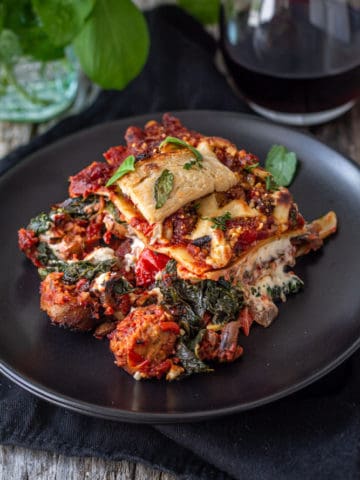 Vegan sausage lasagna on plate with a glass of wine.