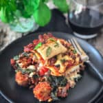 vegan sausage lasagna served on a plate with a fork and a glass of red wine