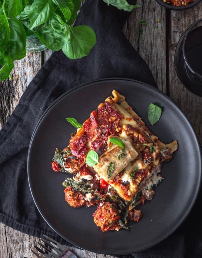 a large piece of vegan sausage lasagna on a plate with a fork and napkin