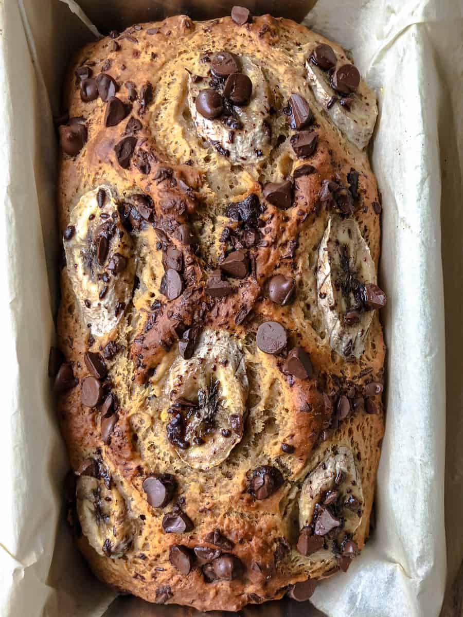 Vegetarian banana bread with melted chocolate chips and banana slices on top in a loaf pan.