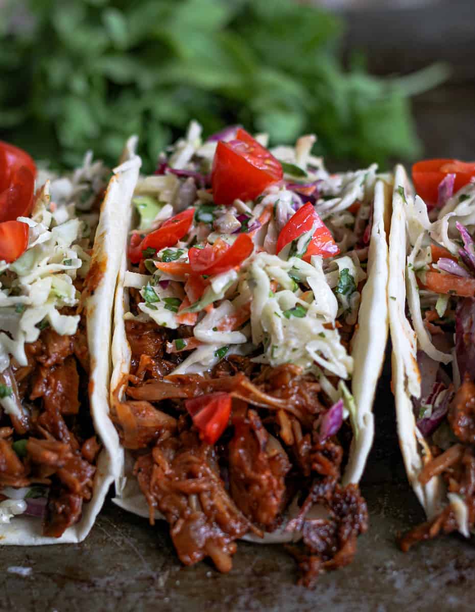 Close up of saucy jackfruit taco with creamy slaw on top and chunks of tomatoes.