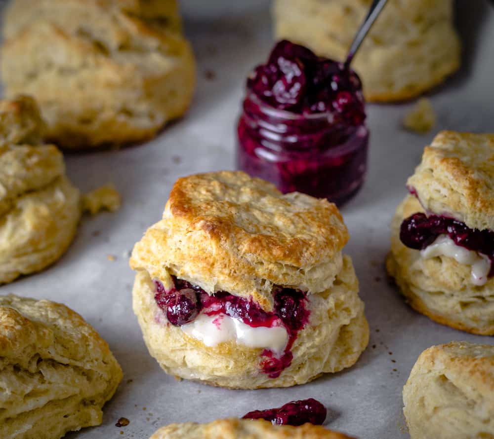 Hot biscuits with melted butter and a jar of jam served on a tray.