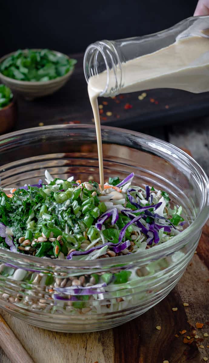 Dressing being pour into a colourful cabbage slaw.