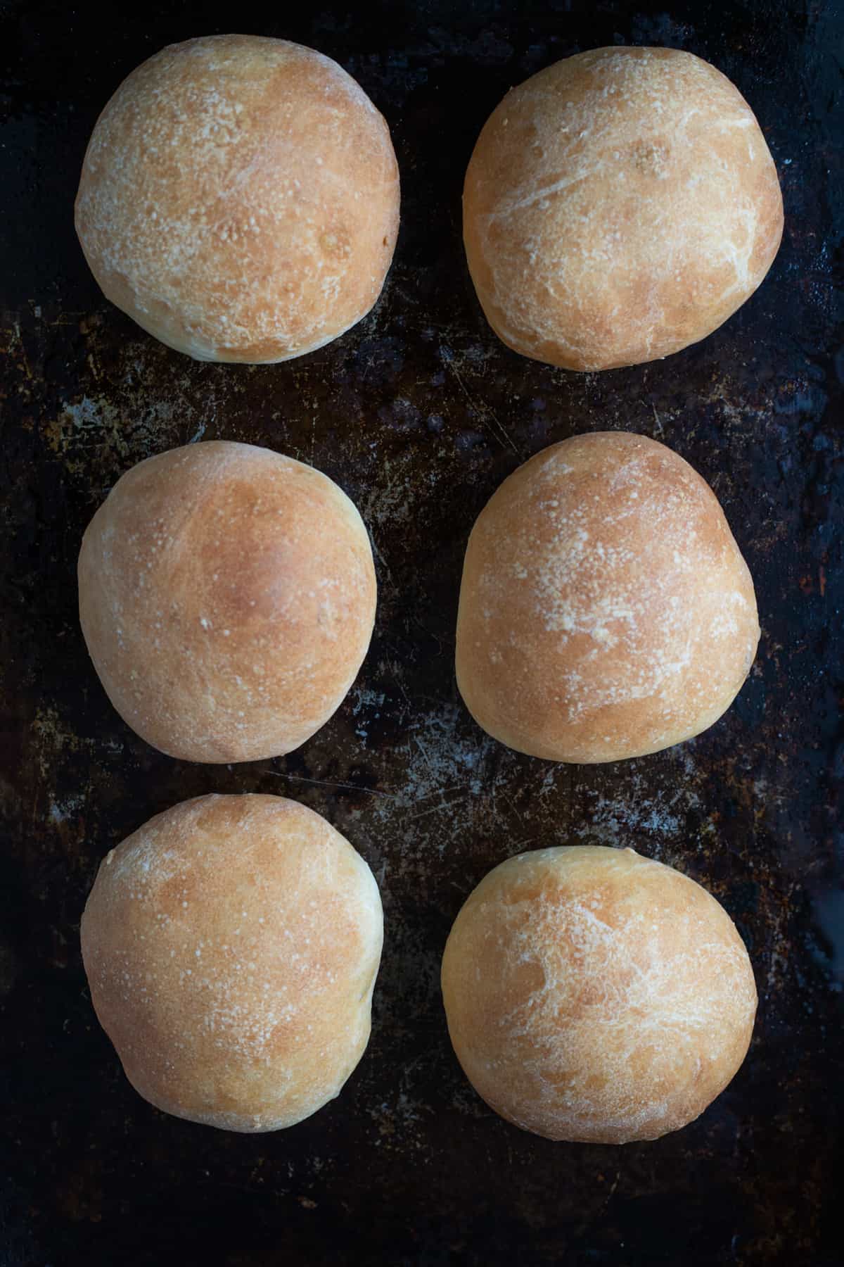 Freshly baked crusty dinner rolls on a baking sheet.