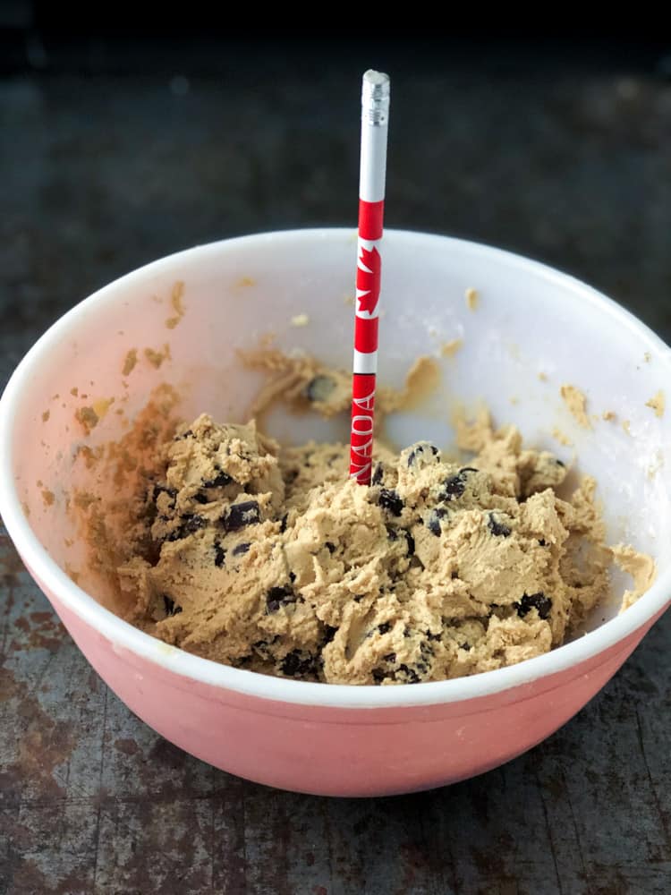 Bowl of stiff chocolate chip cookie dough with pencil stuck in middle.
