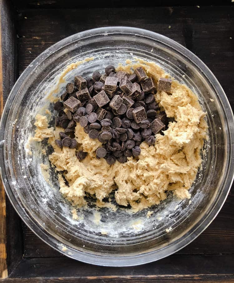 A pile of chocolate chips being mixed into cooking dough in a bowl.