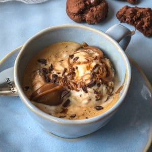 Scoop of ice cream topped with coffee, vegan caramel sauce, and sprinkles of chocolate served in a coffee cup sitting on a saucer.