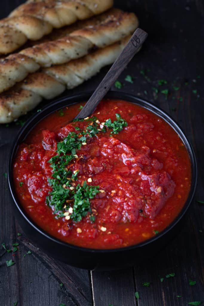 Bowlful of thick, rich red marinar a sauce served with breadsticks.