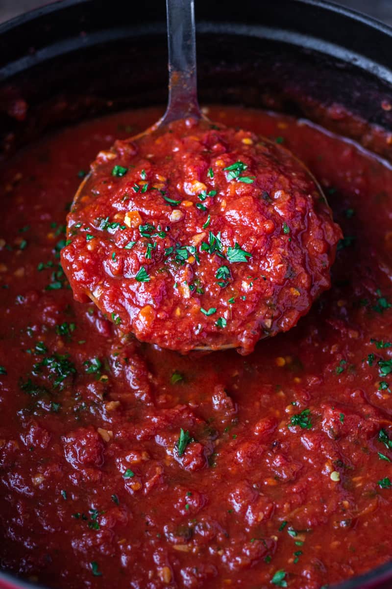 Ladleful of rich red marinara sauce over a pot of sauce.