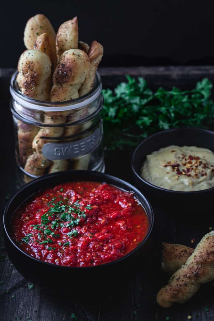 Bowlful of rich red marinara sauce on a tray served with cheese sauce and breadsticks.