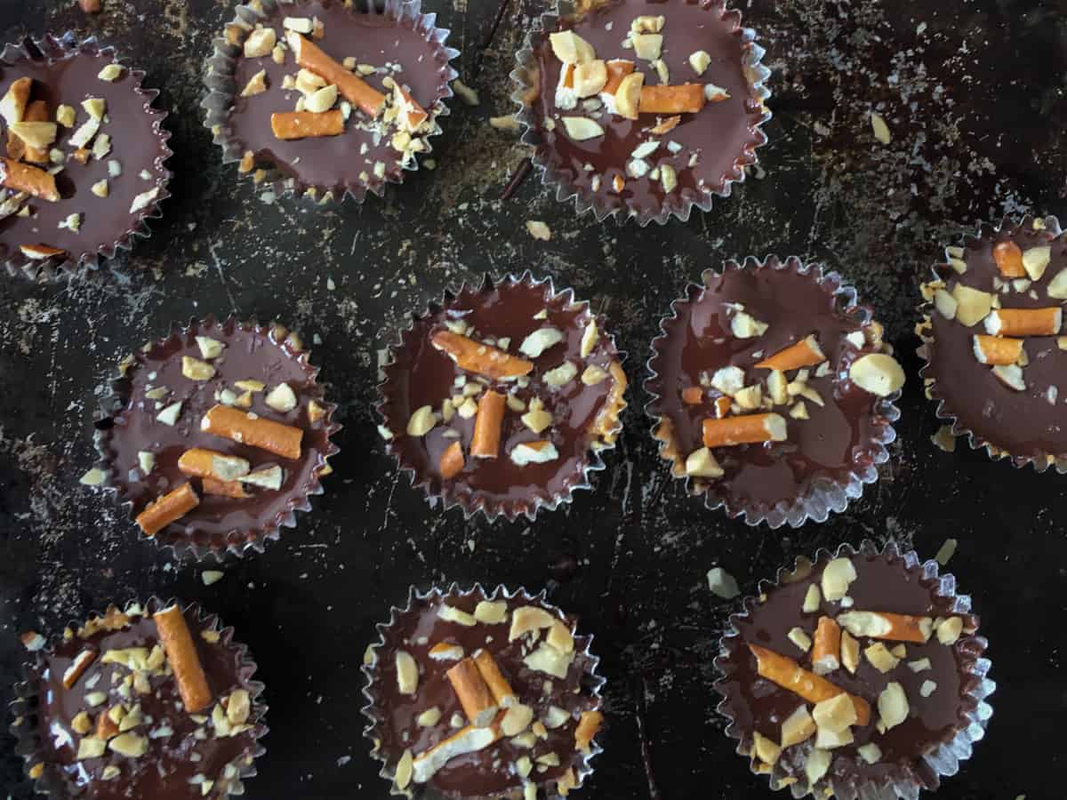 Trayful of mini vegan peanut butter cups with crushed peanuts and pretzels on top.