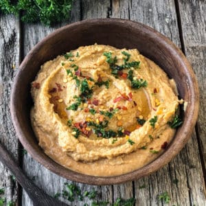 Spicy hummus topped with a swirl of oil, sprinkle of parsley, and red pepper flakes, served on a platter