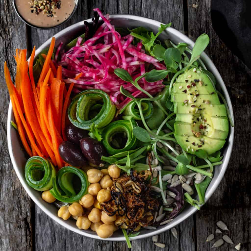 Fresh side salad with cucumber coils, carrots sticks, avocado slices, sprouts and chickpeas served in a big bowl.