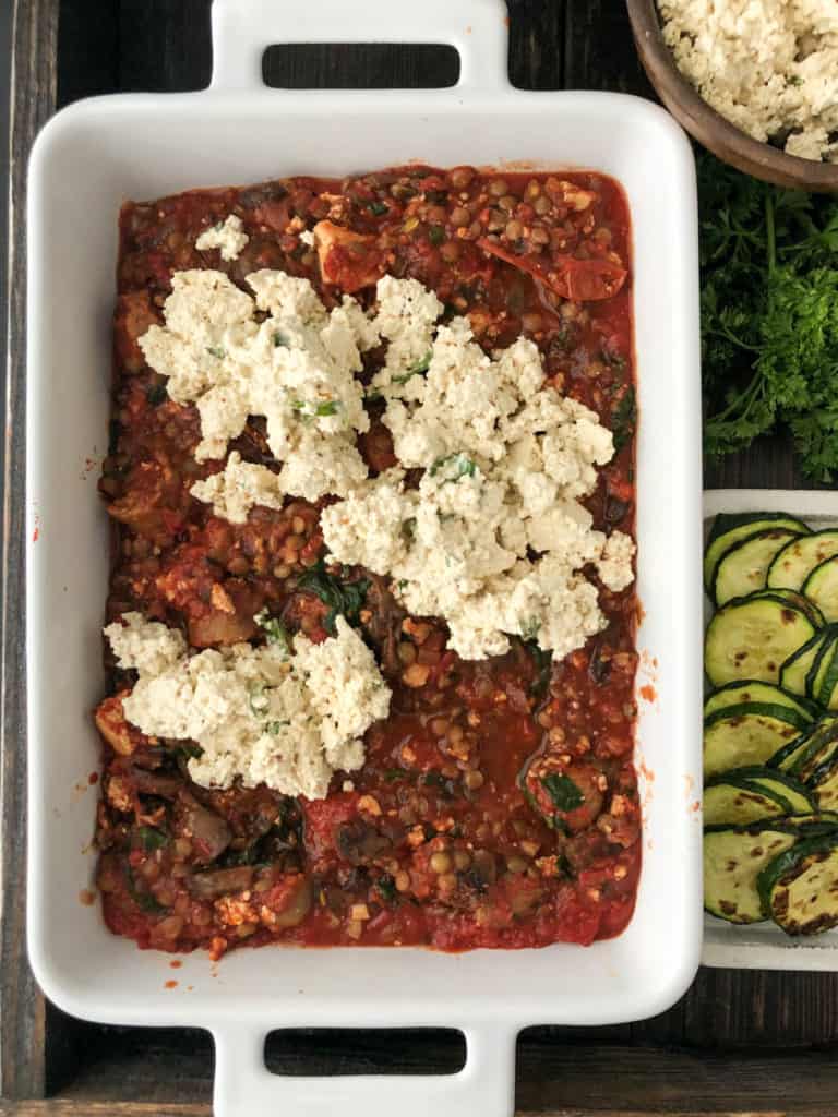 Vegan lasagna being layered with ricotta cheese and sauce.