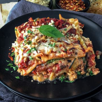 Slice of vegan lasagna on a plate topped with basil leaf.