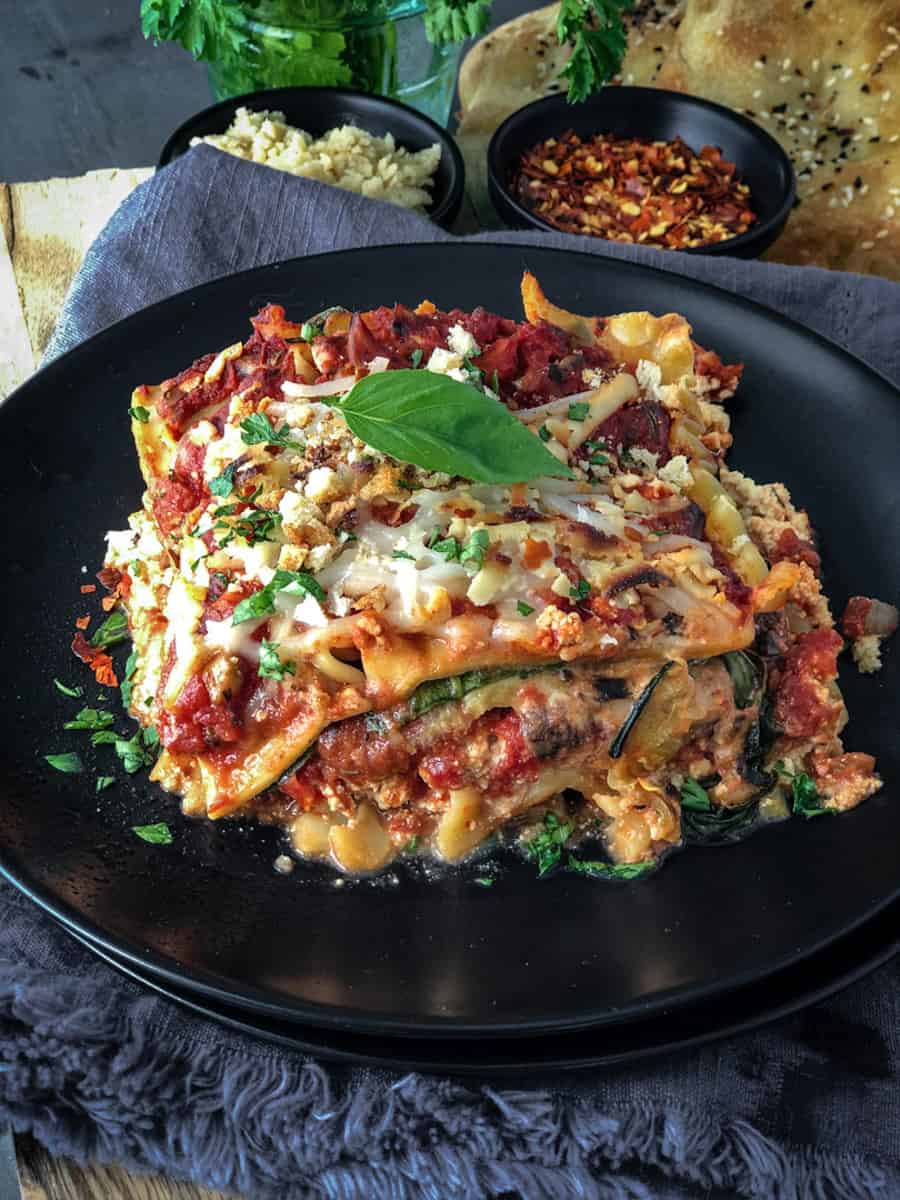 Slice of the best vegan lasagna on a plate topped with basil leaf.