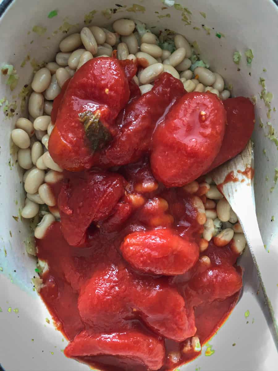 Canned tomatoes being added to vegetable soup.