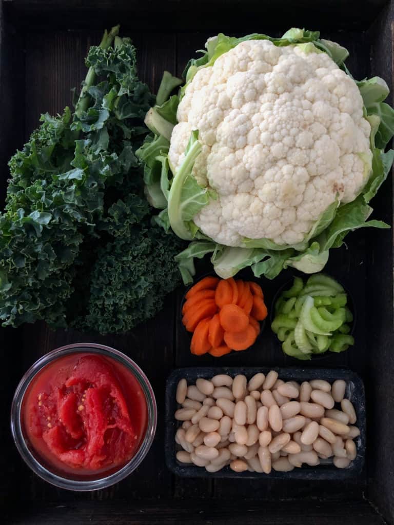Tray of vegetables including cauliflower kale and carrots for vegan bean soup.
